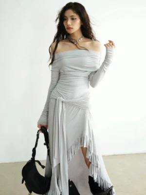 Light grey off shoulder ruched maxi dress shown from a front three quarter angle with extra long sleeves thumbhole cuffs and an asymmetric ruffle hem