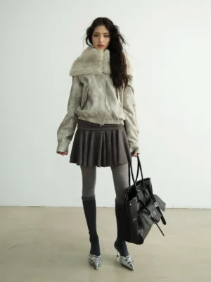 Full front view of an oversized light grey faux shearling hooded streetwear jacket styled with pleated mini skirt and thigh-high socks