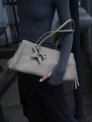 Light grey structured PU leather commuter tote bag carried on the arm with dual star charms and pink tassel detail