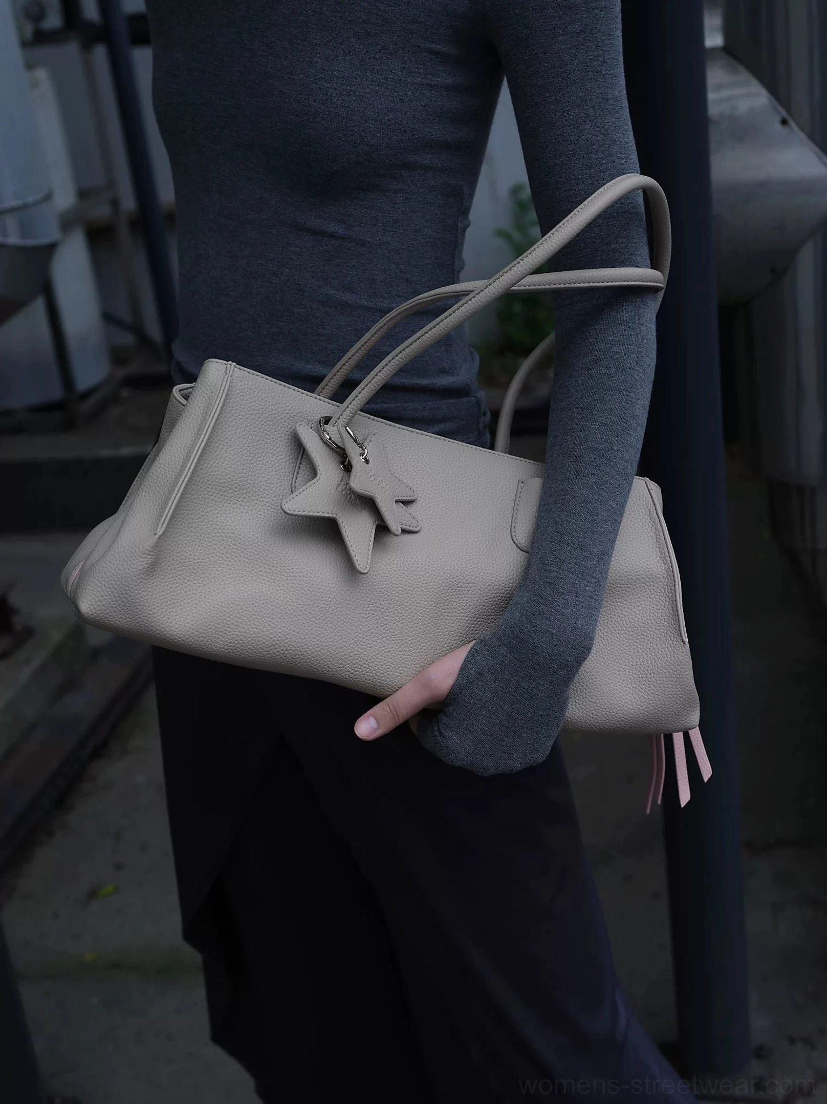 Light grey structured PU leather commuter tote bag carried on the arm with dual star charms and pink tassel detail