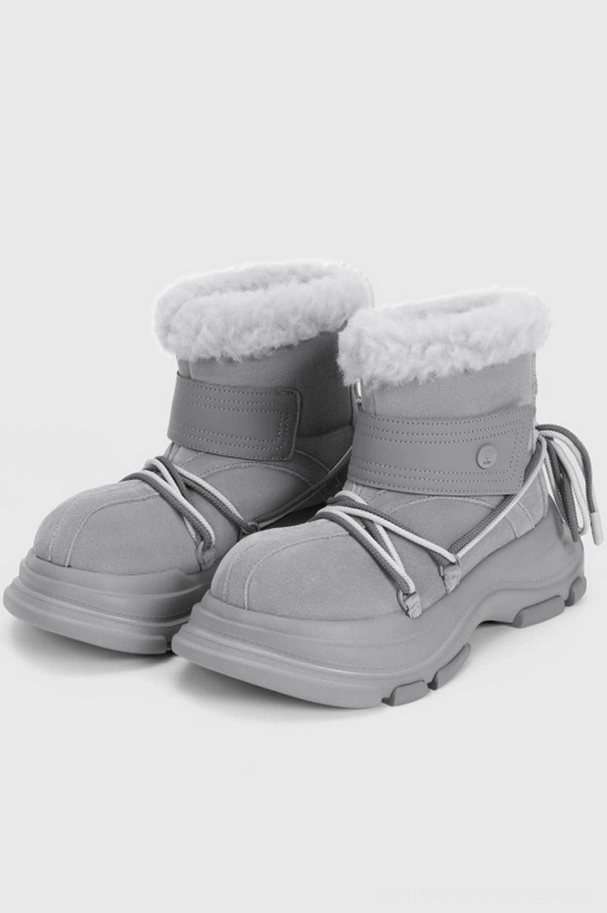 Light grey winter streetwear snow boots in three-quarter view with white faux fur trim, ankle fastening strap, drawstrings, and lug platform sole