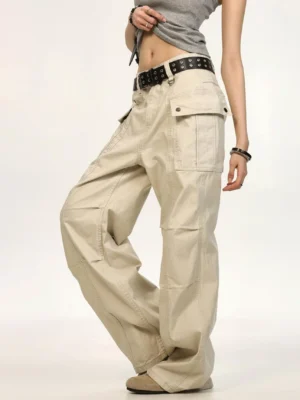 Light khaki beige relaxed wide-leg canvas cargo pants shown from a three-quarter side view with large utility pockets, structured knee creases, and unisex streetwear styling
