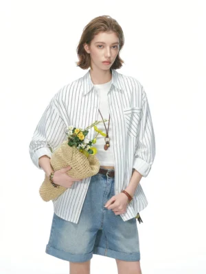 Female model wearing a light khaki relaxed striped shirt over a white T-shirt with denim shorts and a woven flower bouquet