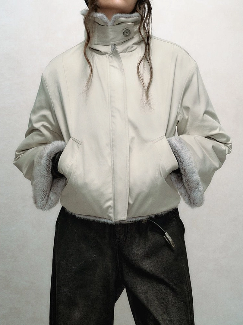 Cropped faux fur bomber jacket in a light neutral shade with stand collar, plush cuffs, hem trim, and slanted side pockets