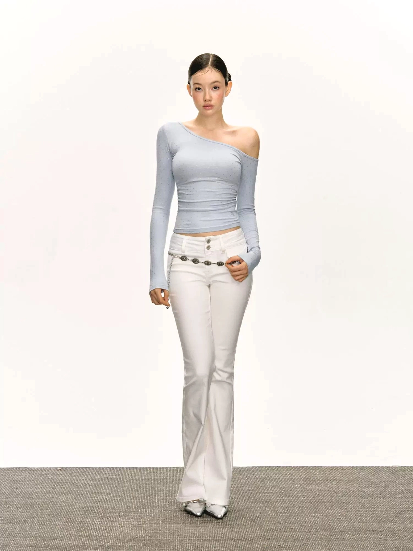 Full-body view of light sky blue asymmetric off-shoulder ruched top styled with white flared pants