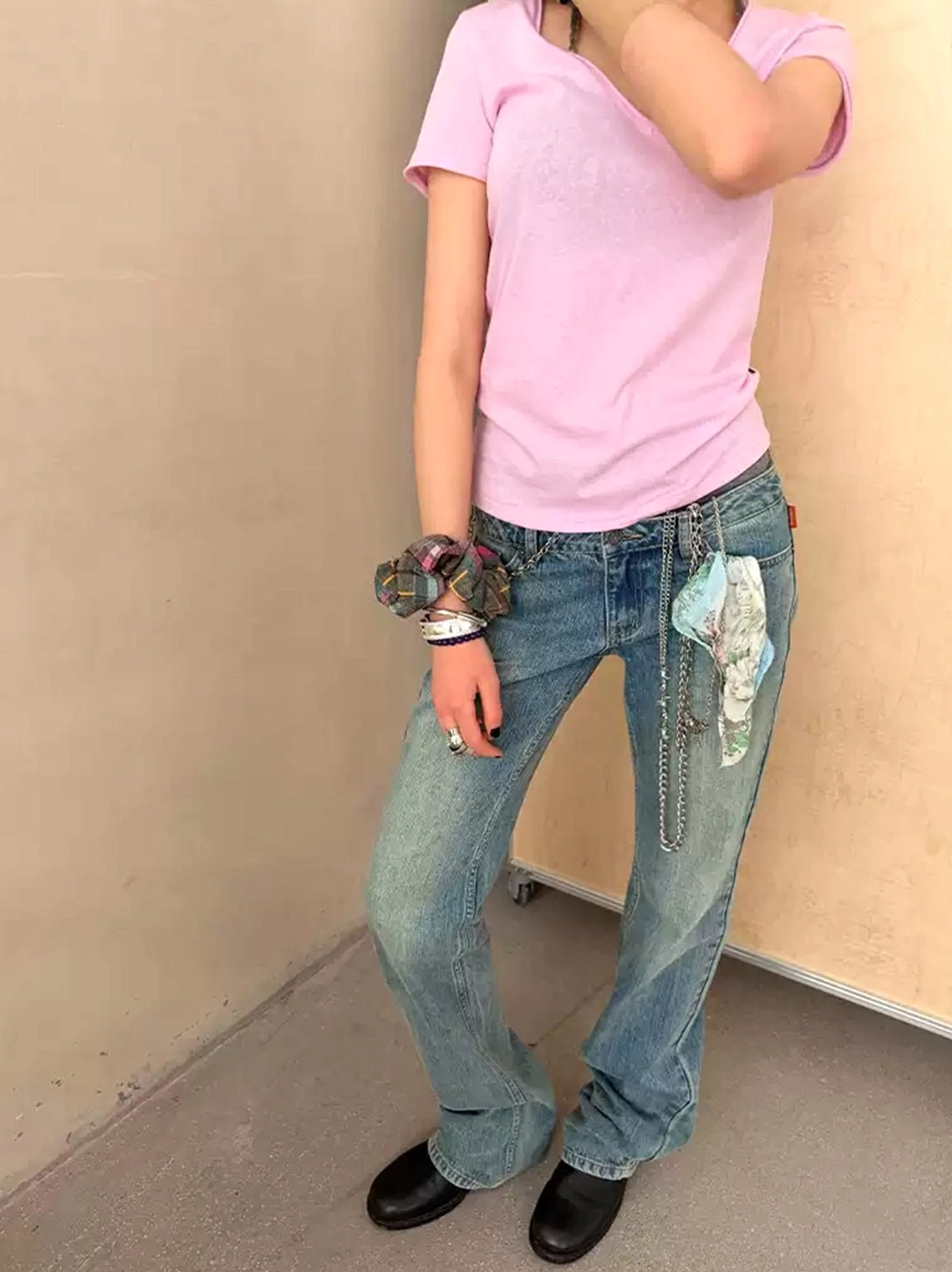 Front partial view of light vintage wash low-rise flare jeans with waist chain, printed fabric decoration, and flared hems