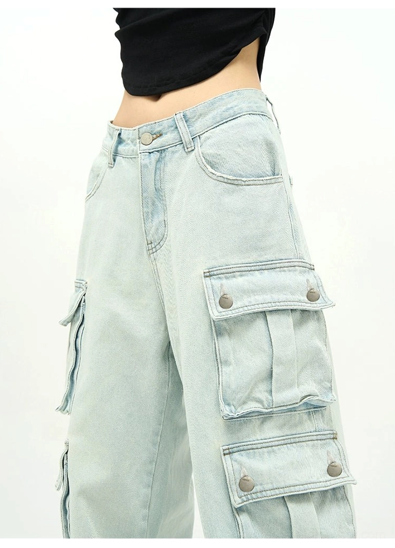 Close-up detail of light wash cotton cargo jeans showing metal snap-button pocket closures, faded denim texture, and utility stitching