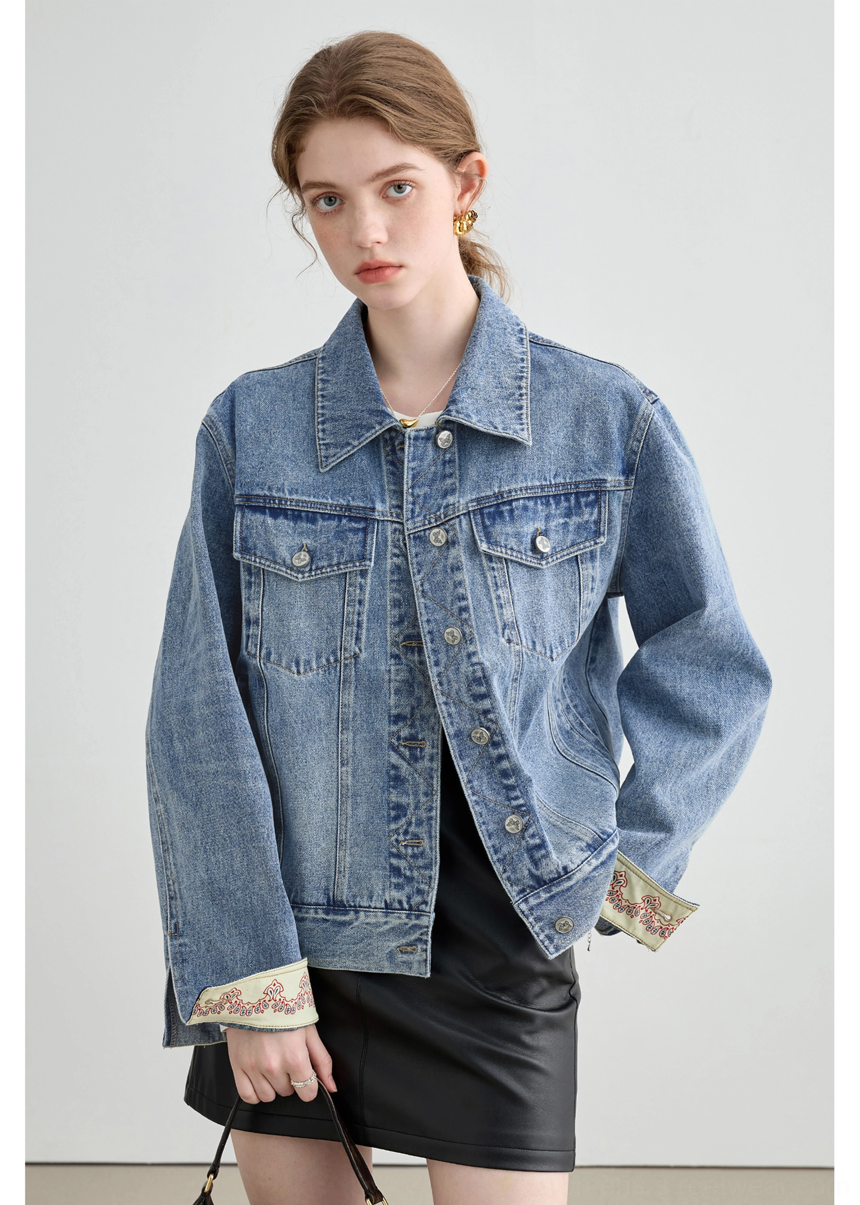 Female model wearing a relaxed light wash denim jacket with patterned embroidered cuffs styled with a black mini skirt
