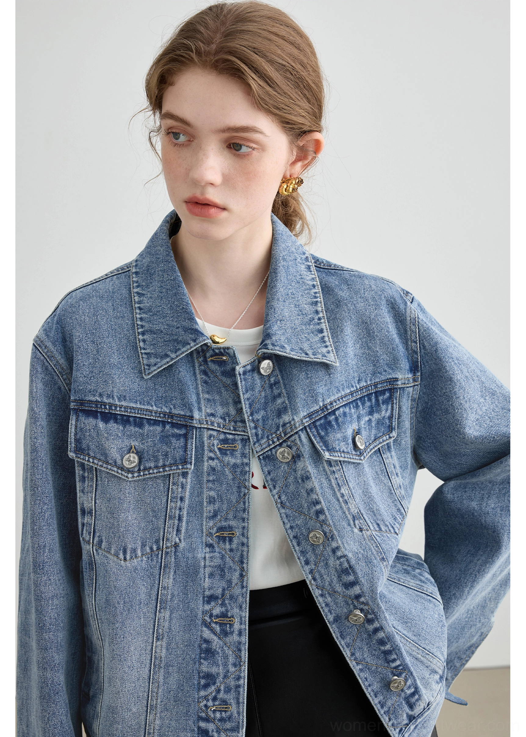 Neck-down close-up of a light wash denim jacket showing metal button front, chest flap pockets, collar, and vintage wash texture