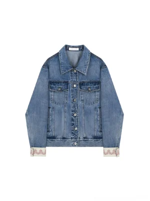 Light wash denim trucker jacket displayed flat with dual chest pockets, button front, and embroidered turn-back cuffs