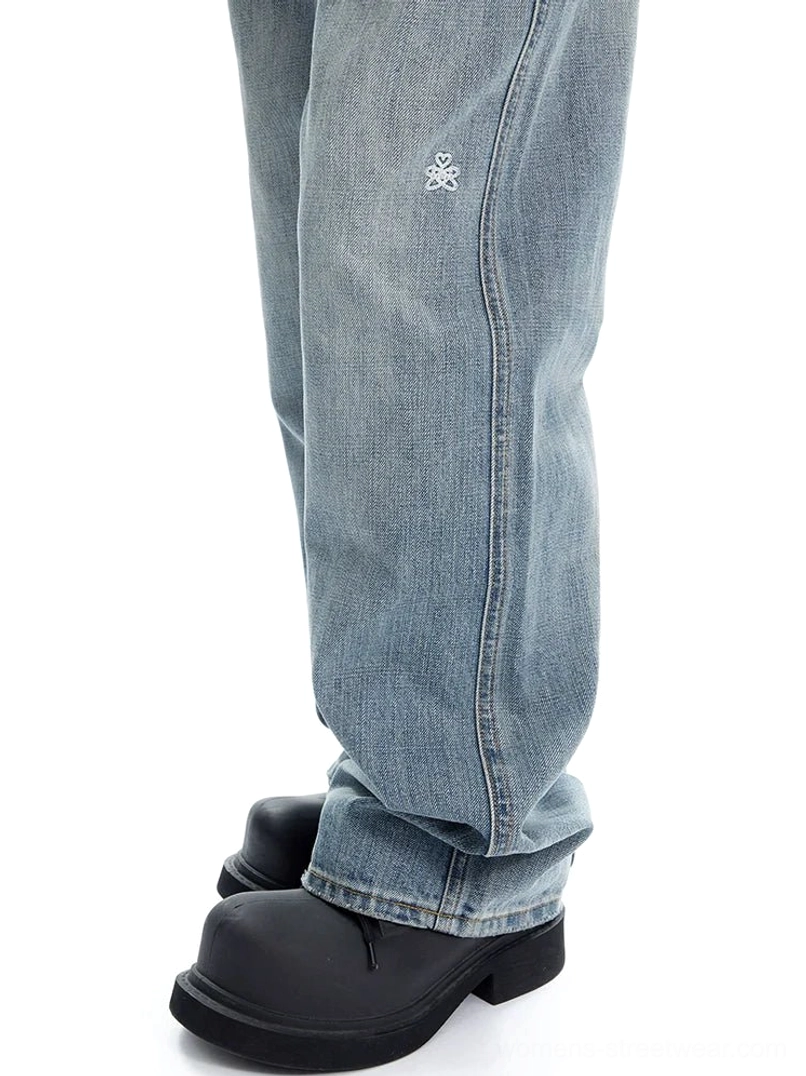 Close-up low-angle detail of light wash wide-leg denim showing cotton-blend texture, seam stitching, and small front-leg embroidery