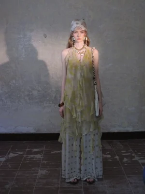 Front view of a lime green sheer ruffle layered halter maxi dress styled with printed wide-leg trousers in a vintage studio
