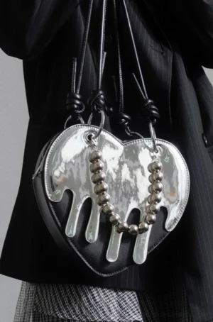 Liquid chrome heart crossbody bag close-up with black melting drip trim, silver bead chain dangle, and knotted black shoulder straps