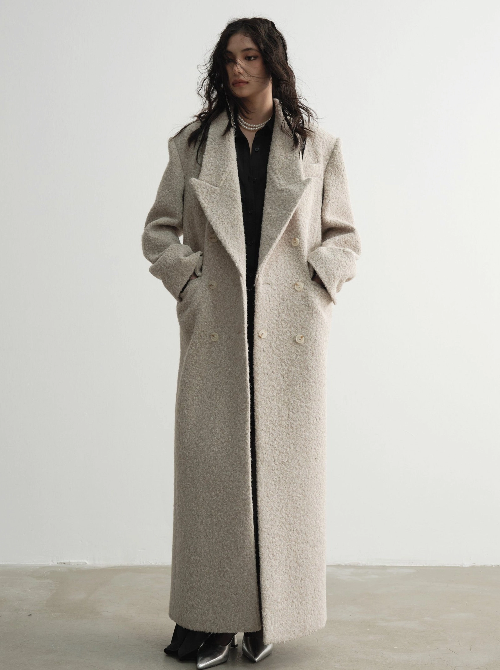 Long oversized bouclé wool coat in oatmeal beige showing double-breasted buttons, floor-length hem and practical pockets