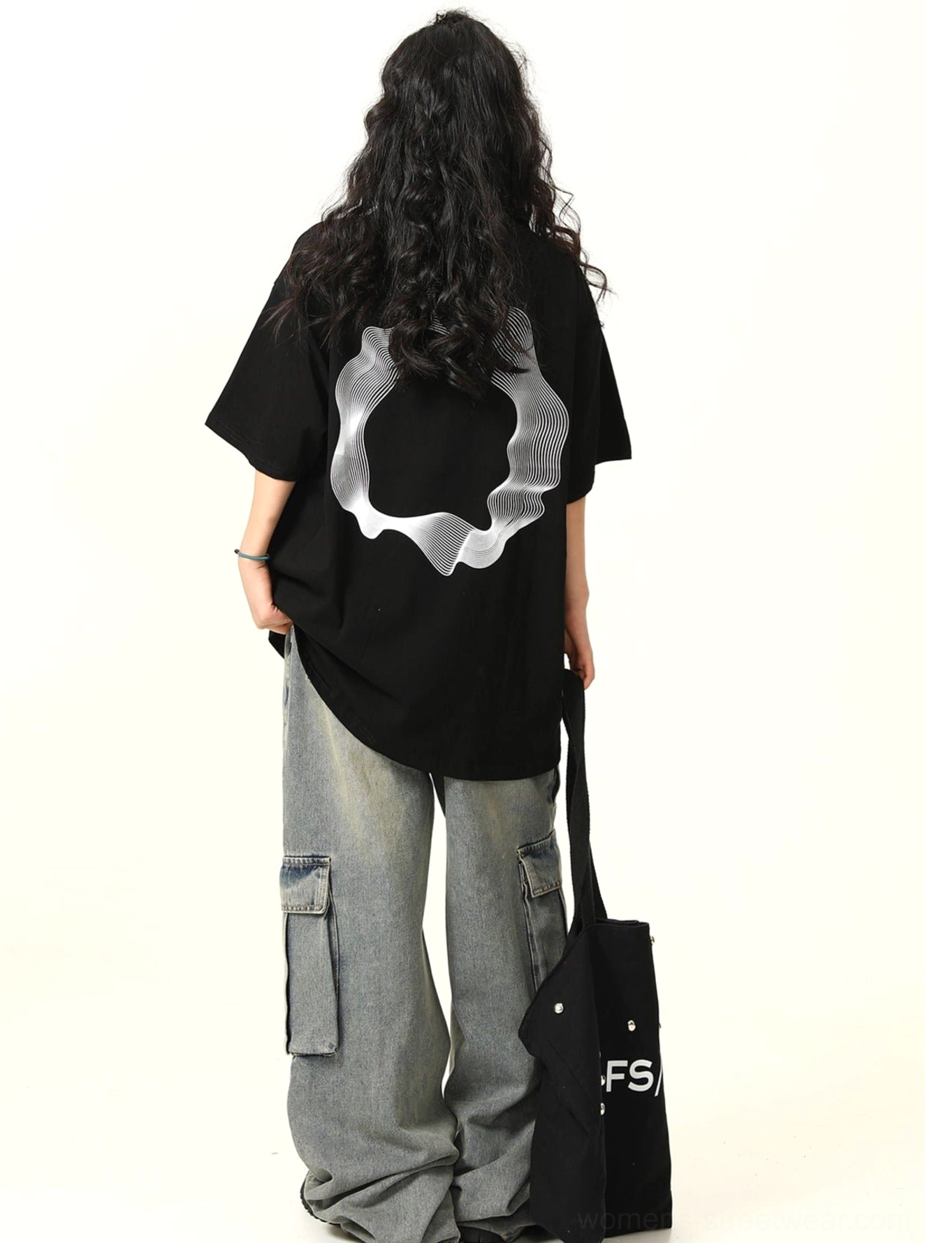 Rear full body view of loose black graphic cotton tee with oversized white wavy ring back print and gray cargo jeans