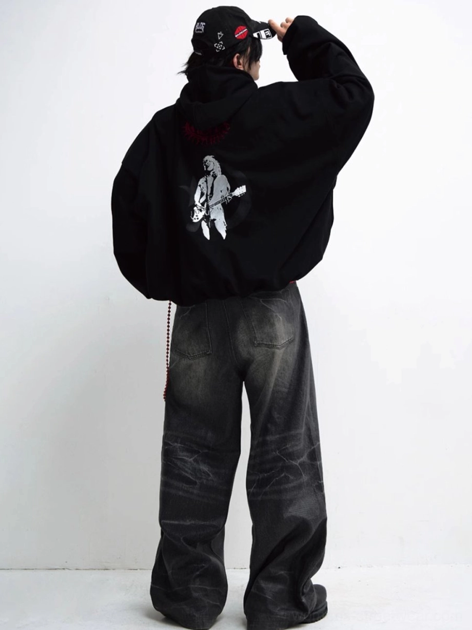 Rear view of a loose black streetwear hoodie featuring a white guitarist back print and red artwork