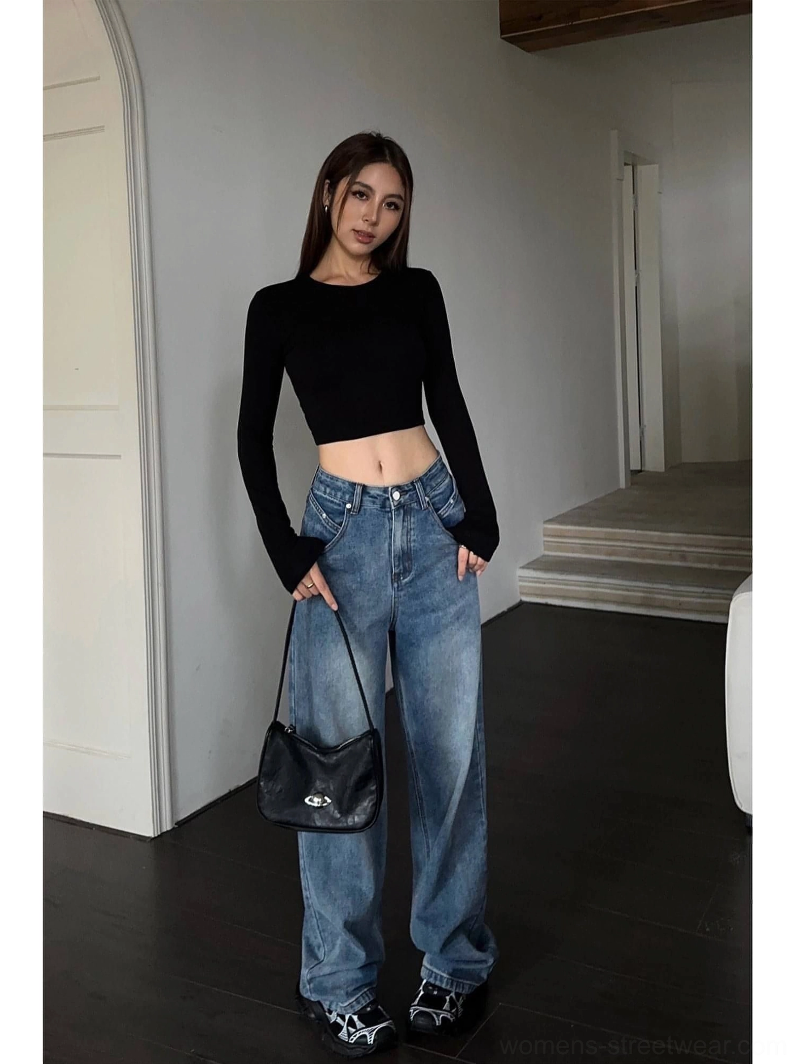 Side-front view of female model wearing loose wide-leg blue washed denim jeans with a black cropped top
