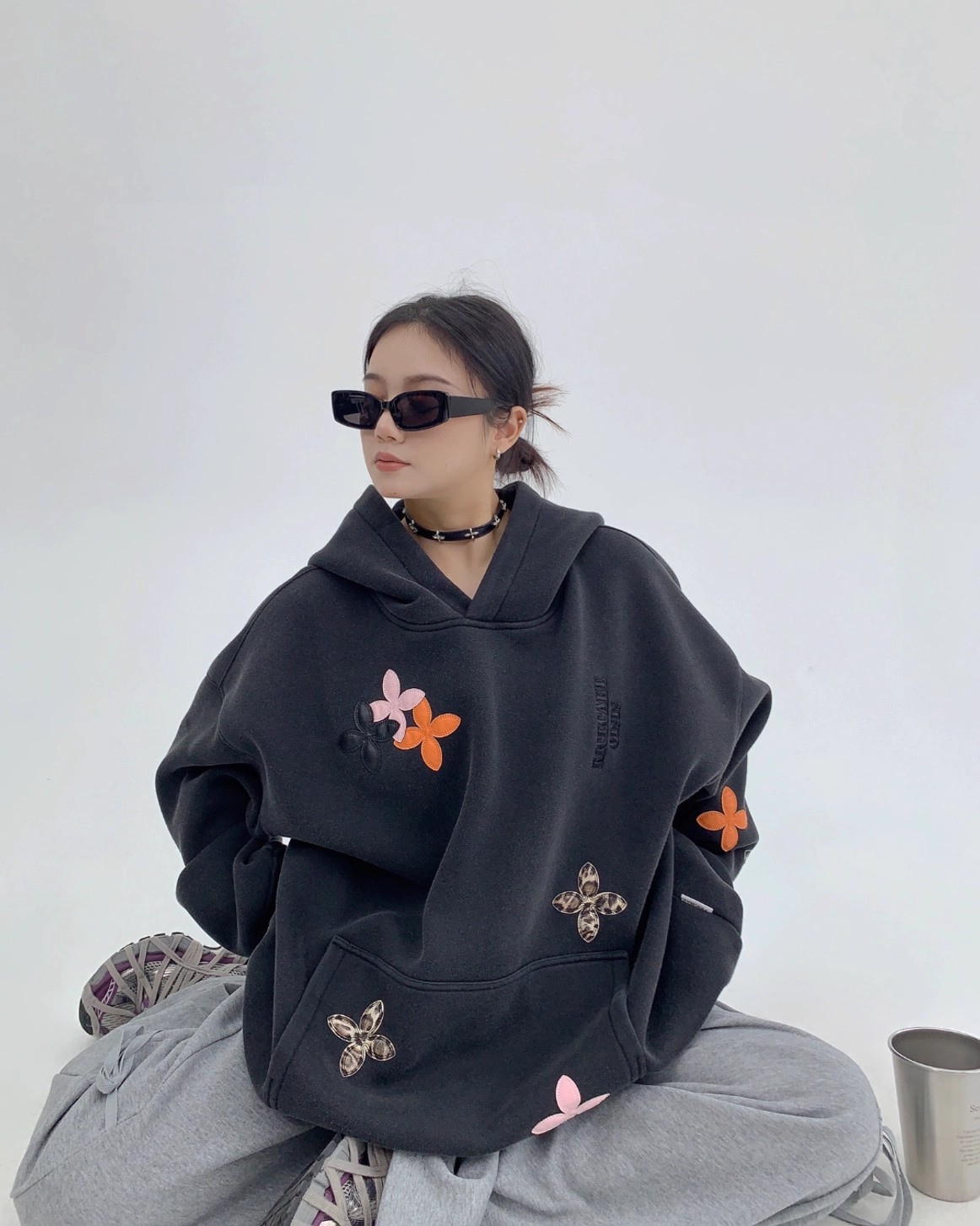 Low-angle front three-quarter view of an oversized black graphic hoodie with colorful floral and leopard-print appliqués in a bold Y2K style