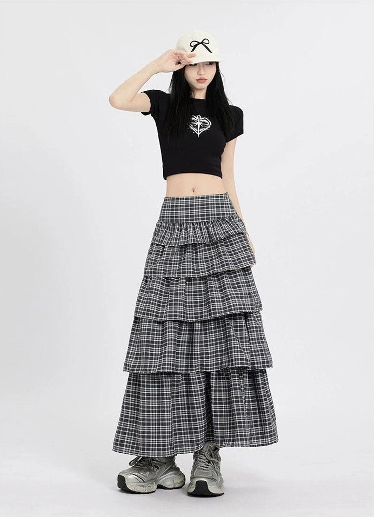Low angle front view of a high waisted dark plaid tiered maxi skirt with a dramatic flowing silhouette and chunky sneakers