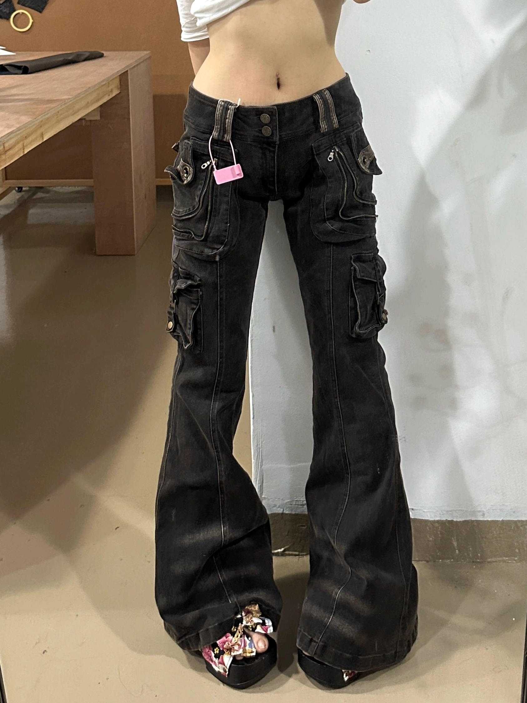 Front lower-body view of low-rise cargo flare jeans with oversized utility pockets, wide flared legs, and pointed floral shoes