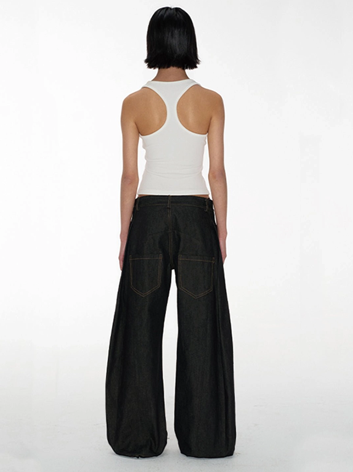 Back view of low-rise curved raw denim jeans showing large rear patch pockets and rounded wide-leg streetwear fit