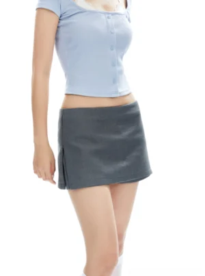 Three-quarter view of a low-rise gray mini skirt with side slit styled with a cropped blue button-front top