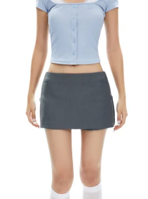 Model wearing a low-rise gray split mini skirt with a cropped blue square-neck top in a minimalist studio streetwear outfit