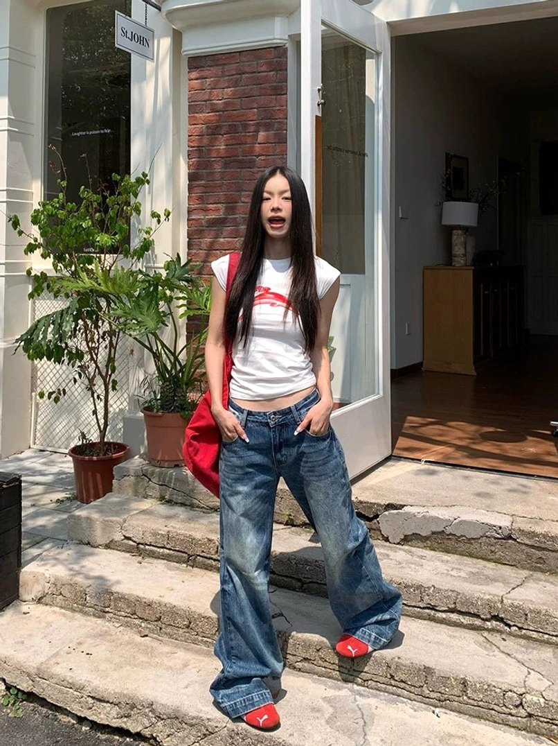 Low-rise wide-leg washed blue jeans styled with a red tote bag and flat shoes on outdoor stone steps