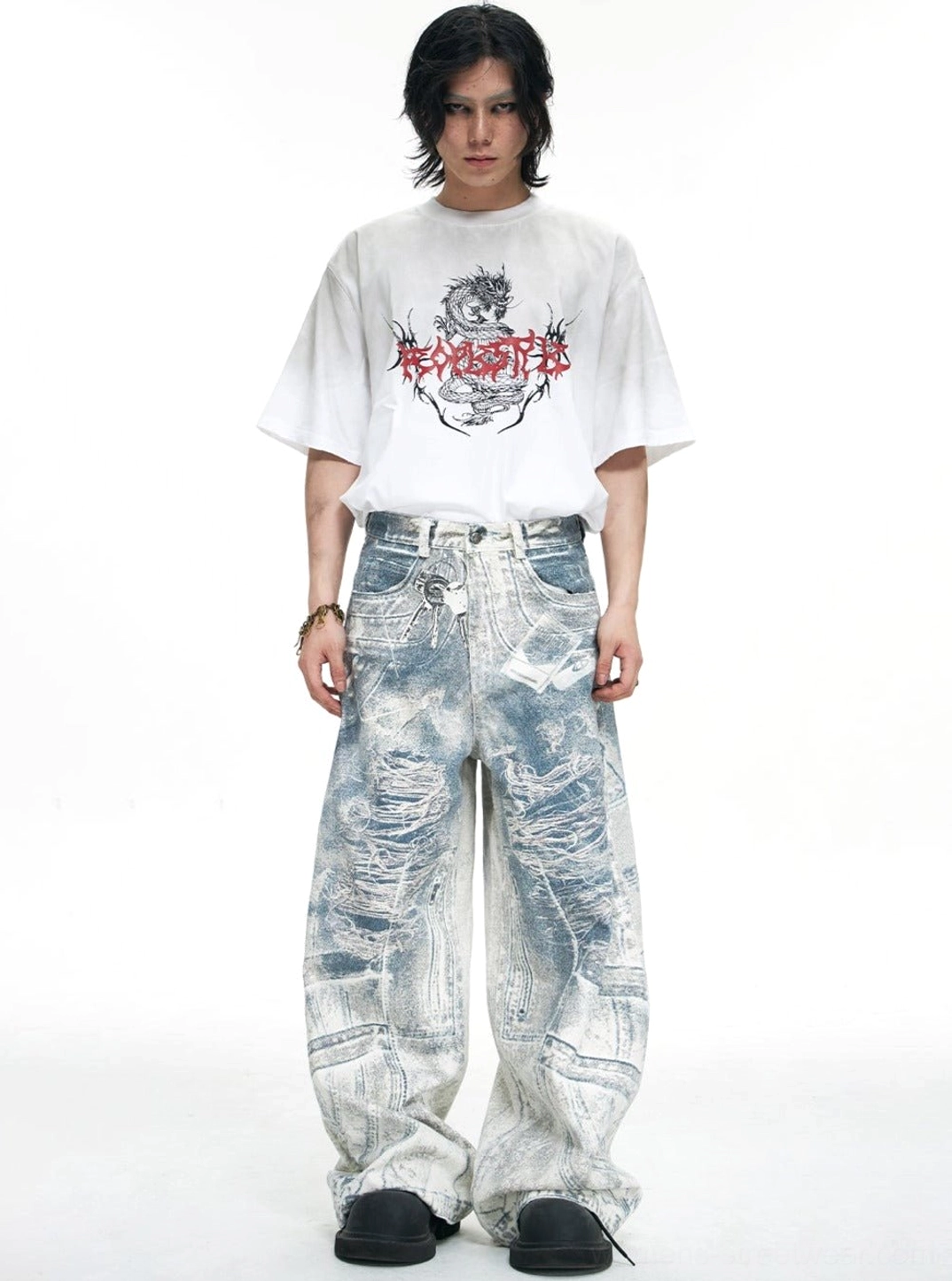 Male model in a graphic white T-shirt styling full-length blue acid-wash distressed baggy jeans for Y2K streetwear