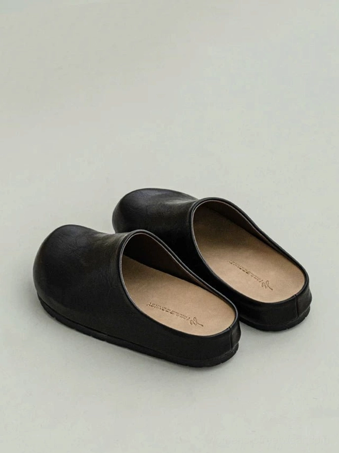 Pair of matte black leather-look closed-toe mule clogs in three-quarter top view with rounded toes and low flat soles