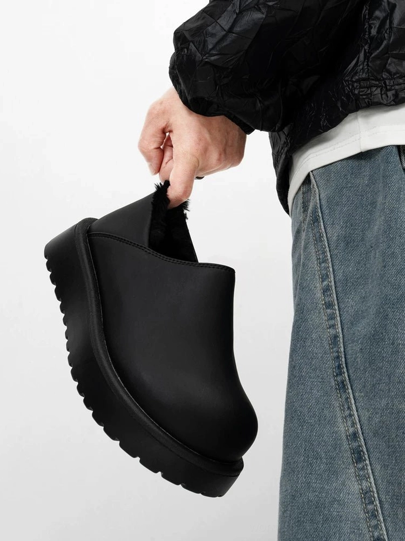 Matte black leather shearling-lined platform clog held in hand, featuring a smooth full-grain upper, chunky black sole, and winter streetwear design