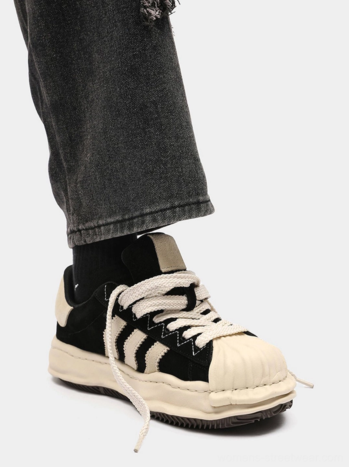 Matte black shell-toe platform sneaker worn with black socks and ripped black jeans, highlighting the chunky melted sole profile