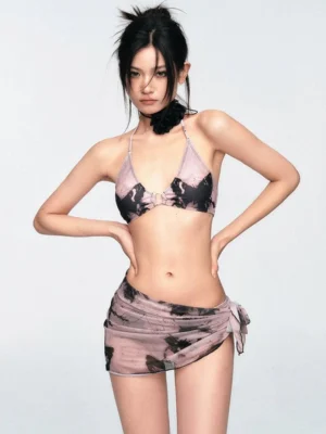 Front three-quarter view of mauve and black tie-dye bikini set with halter triangle top decorative ring and matching wrap sarong skirt