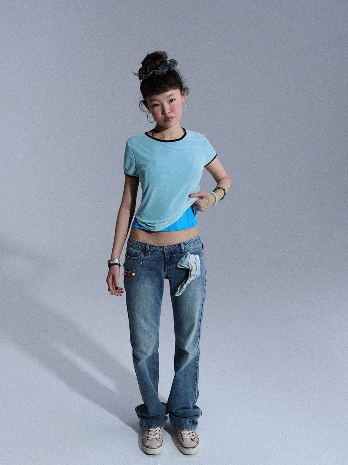 Front full-body view of medium blue low-rise slim flare jeans styled with a light blue cropped top and casual shoes