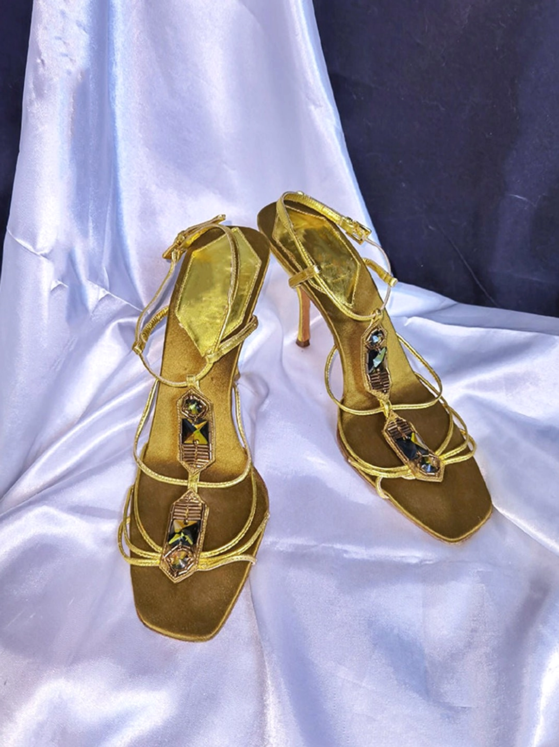 Metallic gold rhinestone square-toe strappy sandals shown from an angled view with slim straps and sparkling decorative hardware