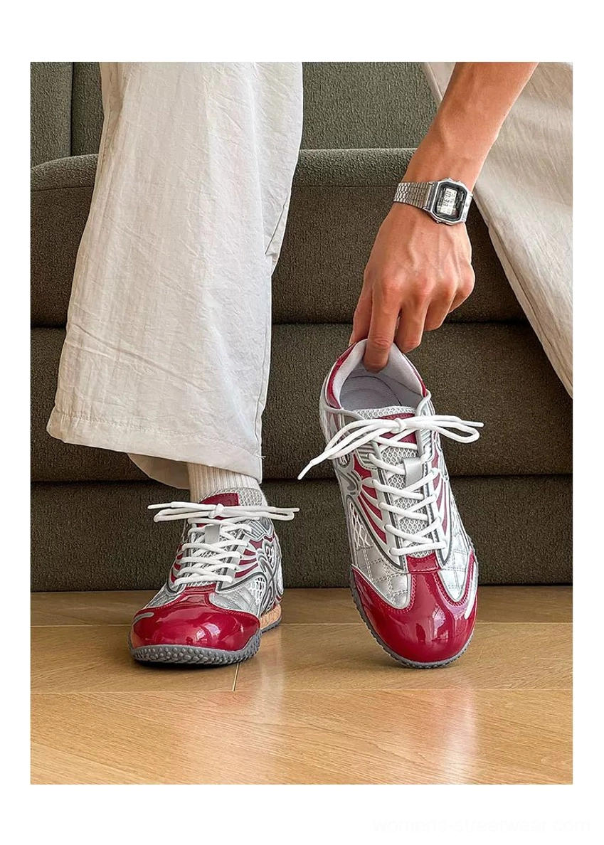 Lifestyle image of metallic red and silver heart mesh retro sneakers worn with off-white pants while sitting indoors on a brown sofa