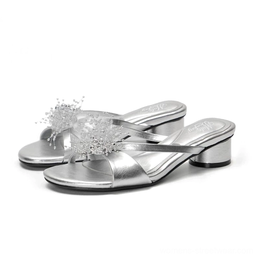 Metallic silver crystal flower crossover low block heel mules displayed in a white studio flat lay