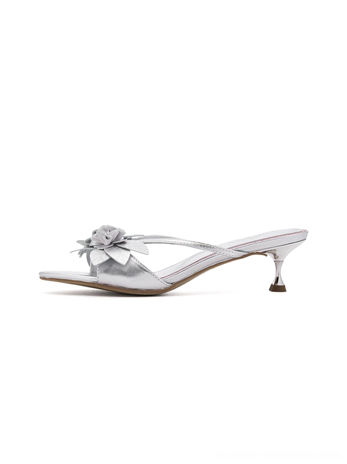 Metallic silver floral kitten heel slide sandals shown in a left side studio view with slim crisscross straps, dimensional flower embellishment, open toe, and tapered low heel
