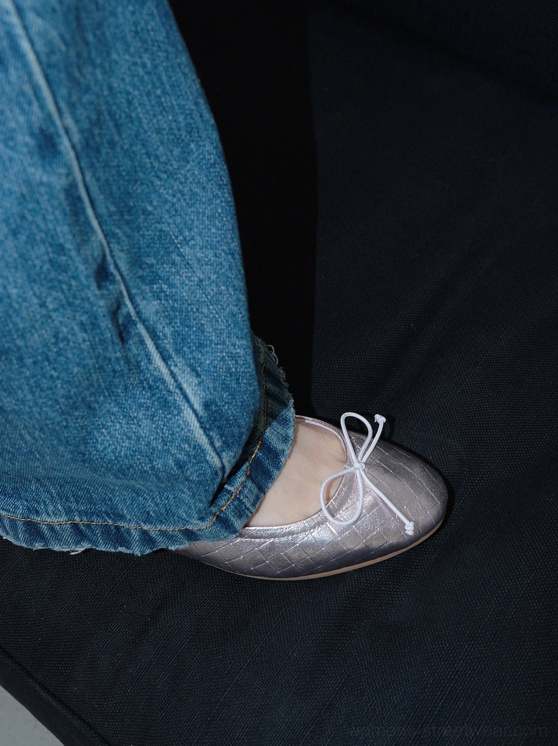 Close up of a metallic silver quilted bow ballet flat paired with blue denim jeans