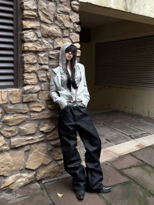 Black metallic raw straight jeans worn in a full front view with a hooded jacket in an urban stone alley