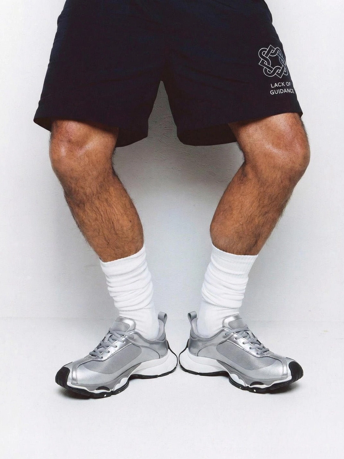 Metallic split-toe technical runner sneakers shown on foot from the front with white crew socks and a modern casual streetwear outfit
