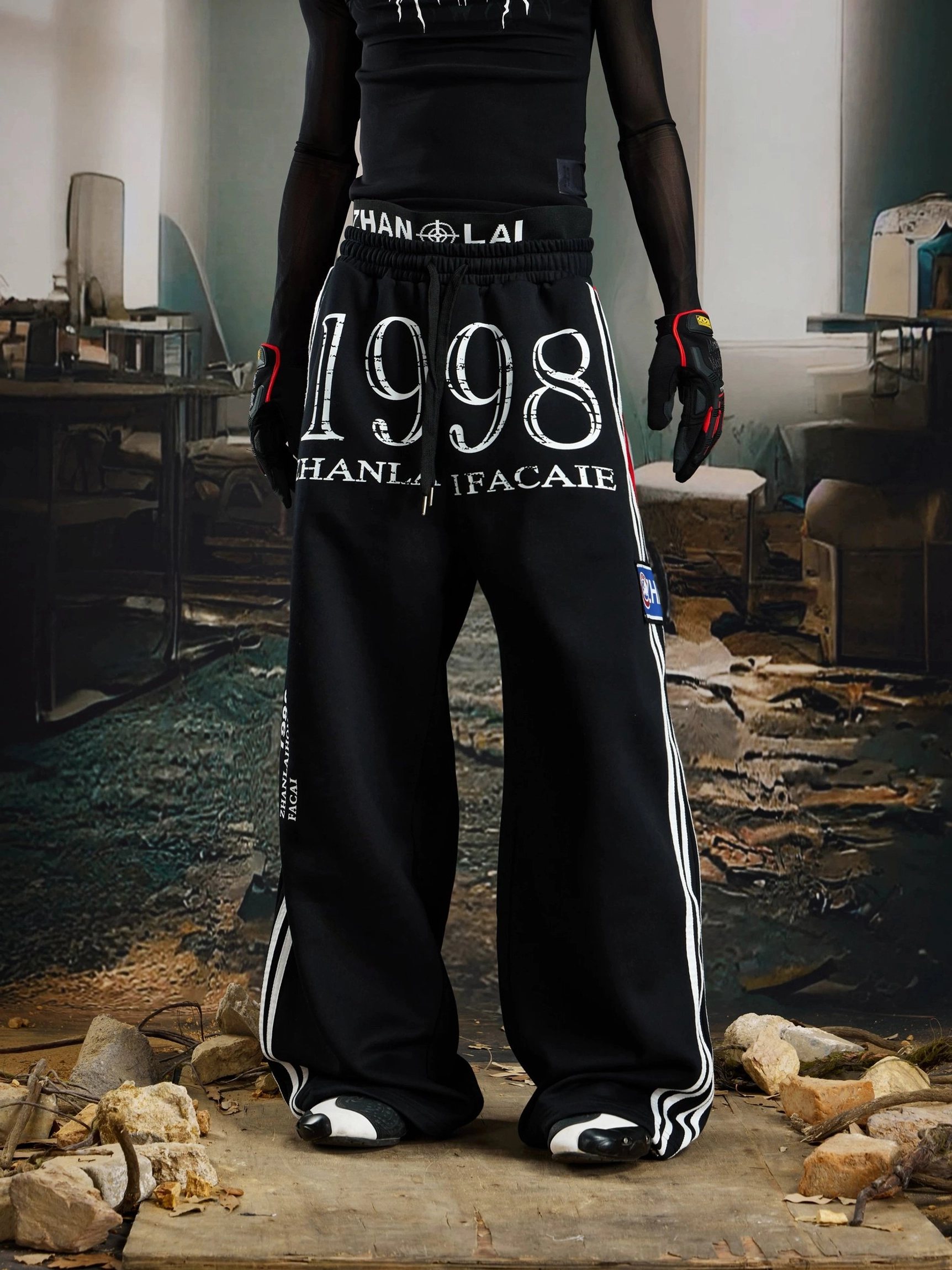 Black 1998 graphic streetwear sweatpants product view showing the wide-leg cut, elastic drawstring waist, white stripes, and patch details
