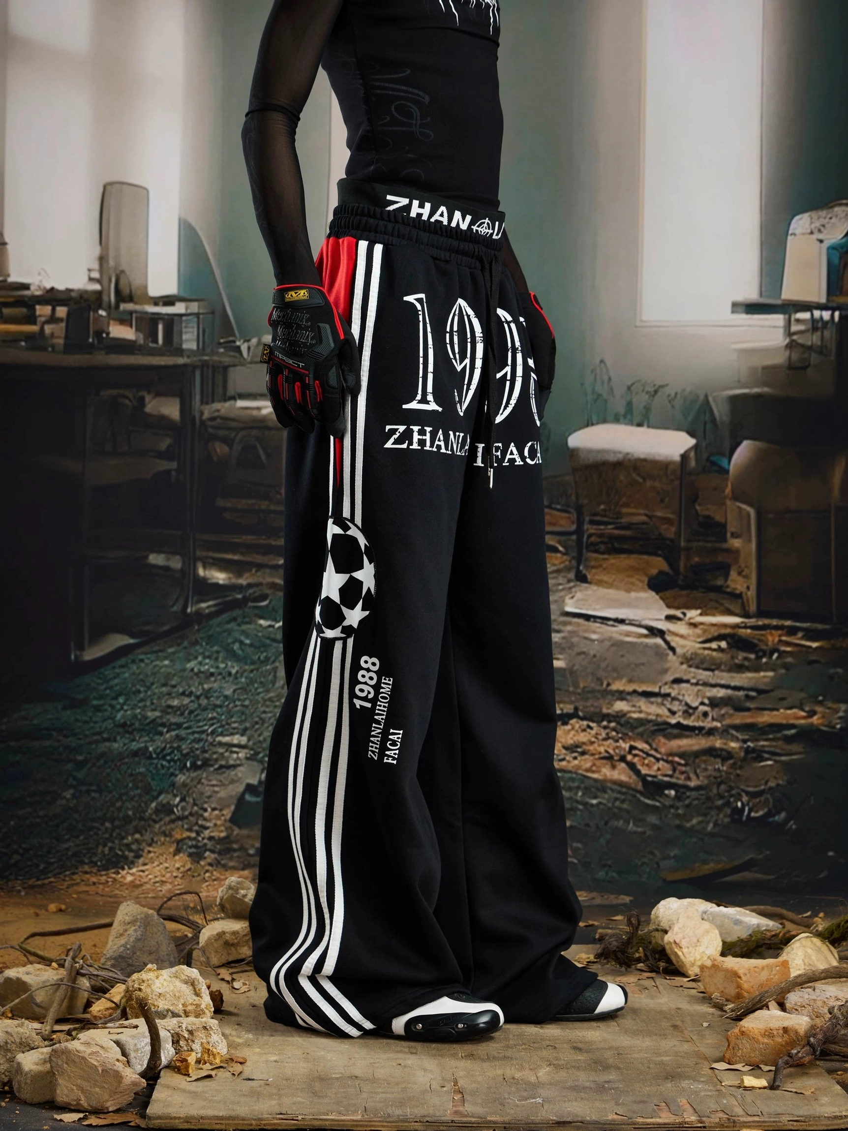Side profile of black graphic streetwear pants featuring white athletic stripes, distressed 1998 print, and soccer-inspired thigh patch
