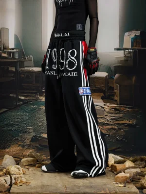 Black 1998 graphic wide-leg streetwear sweatpants shown from a low front angle with white side stripes, distressed lettering, and utility patch details