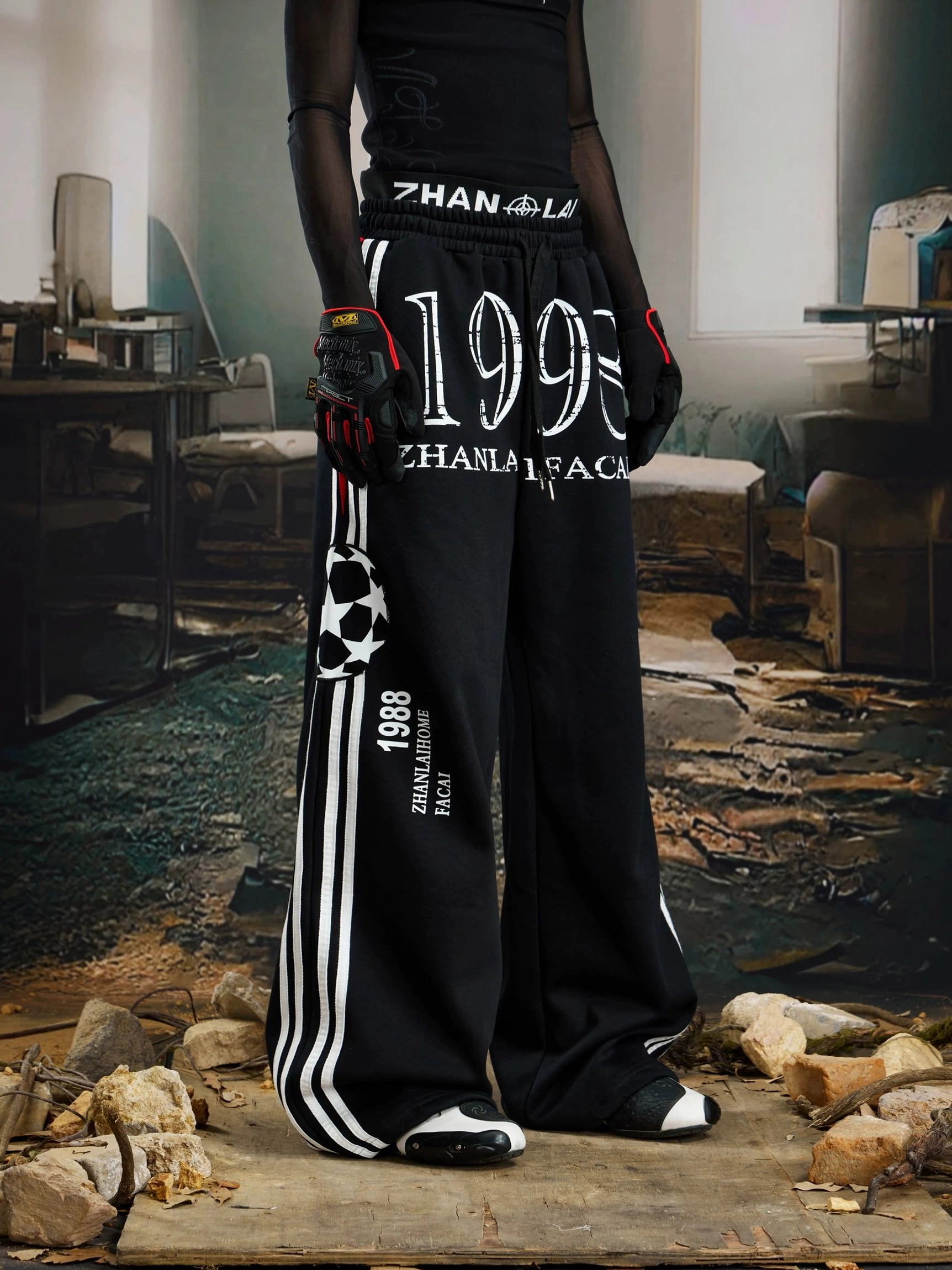 Front view of black oversized graphic sweatpants with large 1998 print, white side stripes, and sporty utility patch details