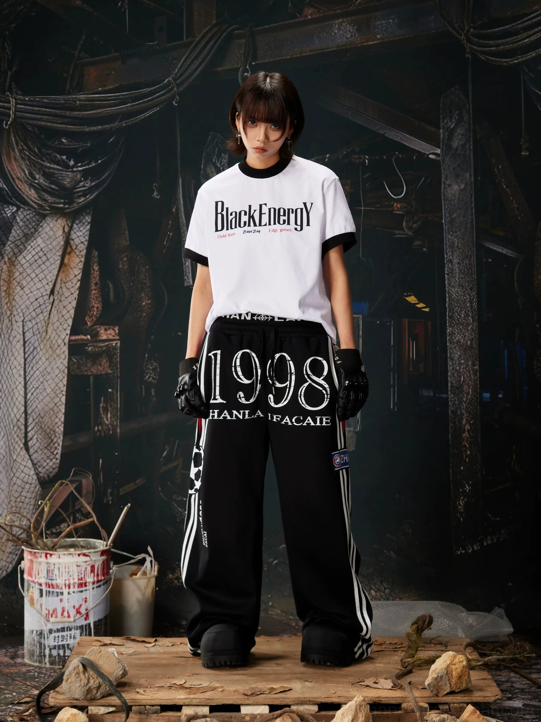 Female model wearing black 1998 graphic wide-leg sweatpants with white side stripes styled with a cropped graphic streetwear tee