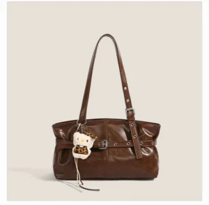 Vintage brown faux leather shoulder bag with belt buckle detail and playful animal pendant showing a glossy worn texture