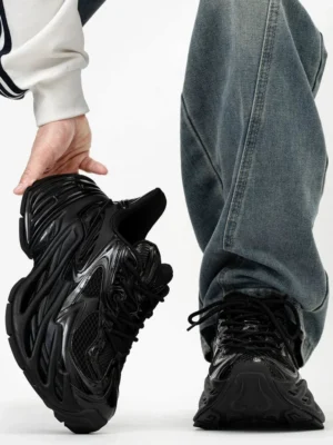 All black Midnight Flux futuristic blade platform sneakers held with baggy blue jeans, showing glossy layered upper, breathable mesh panels and ridged chunky sole