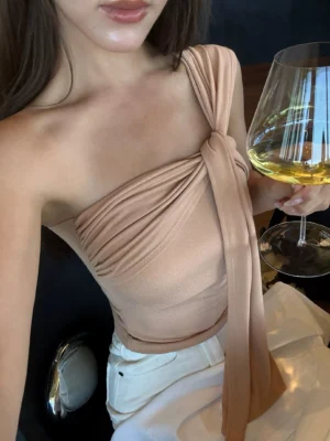 Milk Tea beige asymmetric draped one-shoulder crop top with long shoulder sash and soft stretch fit styled for an elegant evening