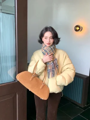Milk yellow cropped duck down puffer jacket with high stand collar, quilted volume, front zipper and relaxed streetwear fit styled with a plaid scarf and brown corduroy trousers